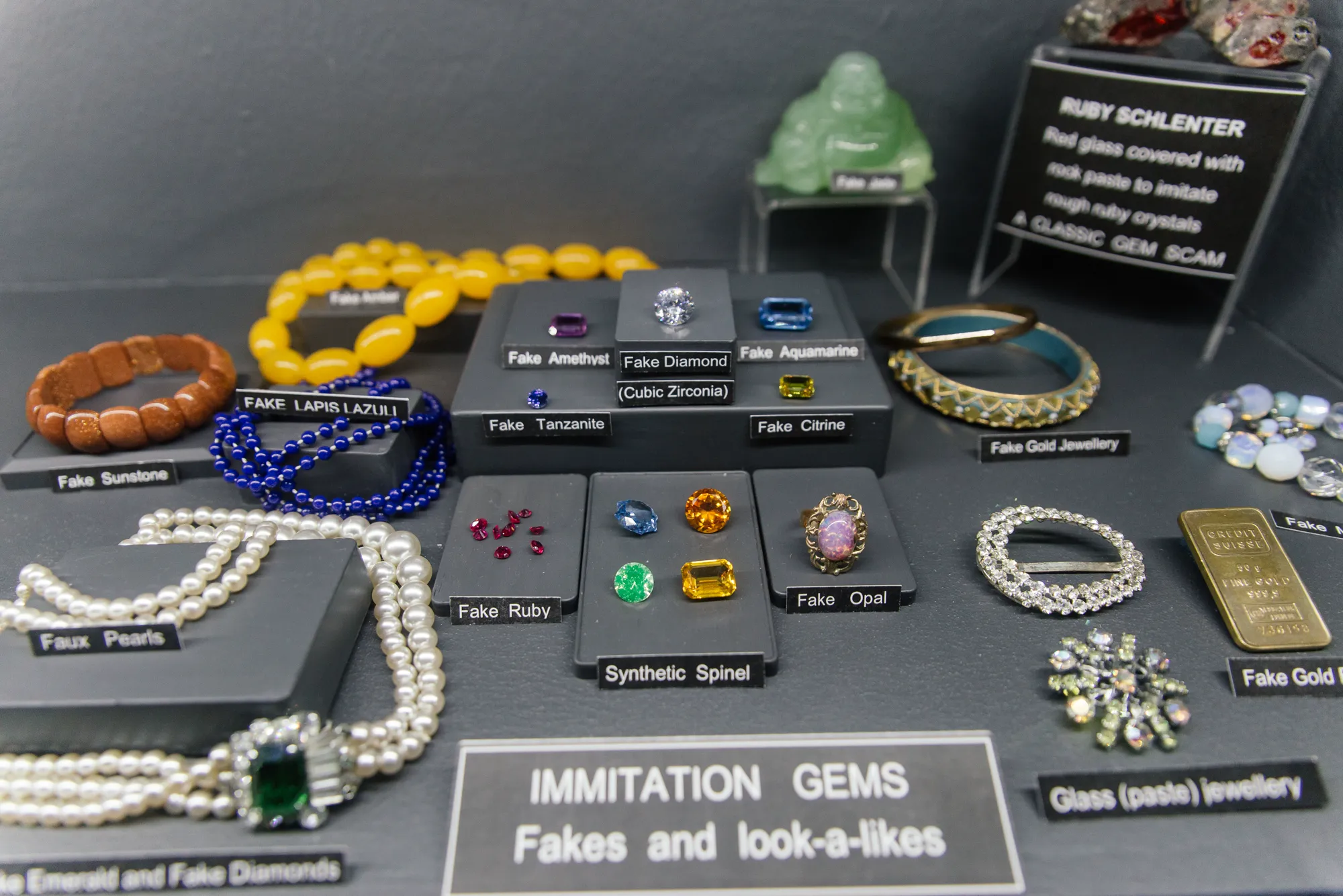The imitation-gems cabinet in the museum: synthetic spinel, cubic zirconia (fake diamond), ruby schlenter, fake amber, fake lapis lazuli, faux pearls, fake jade Buddha, fake gold bars and dyed beadwork laid out beside their natural counterparts