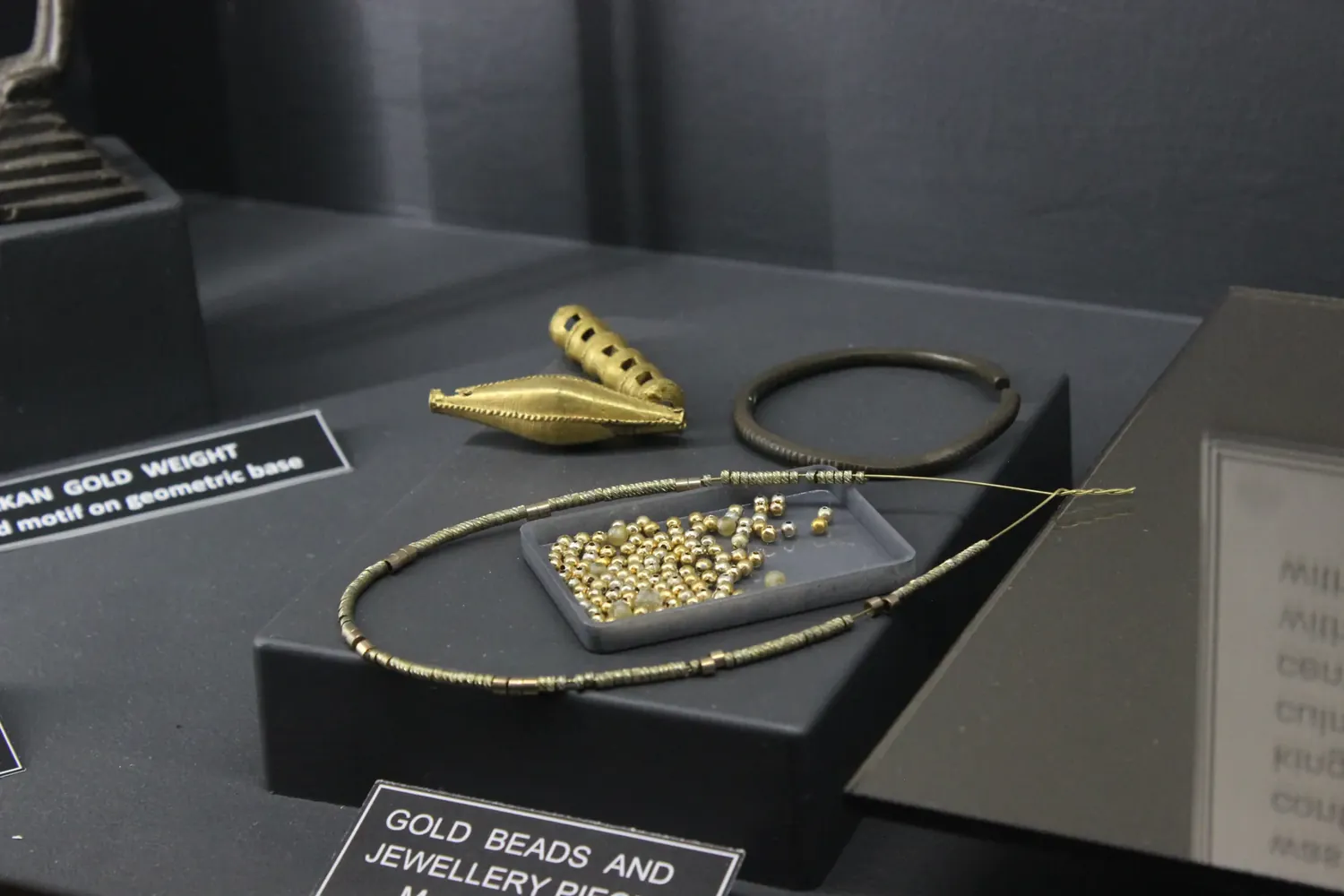 Gold beads and jewellery pieces in a Space C showcase: a tray of loose gold beads, a strand of fine wire beads, two large gold beads and a metal bangle