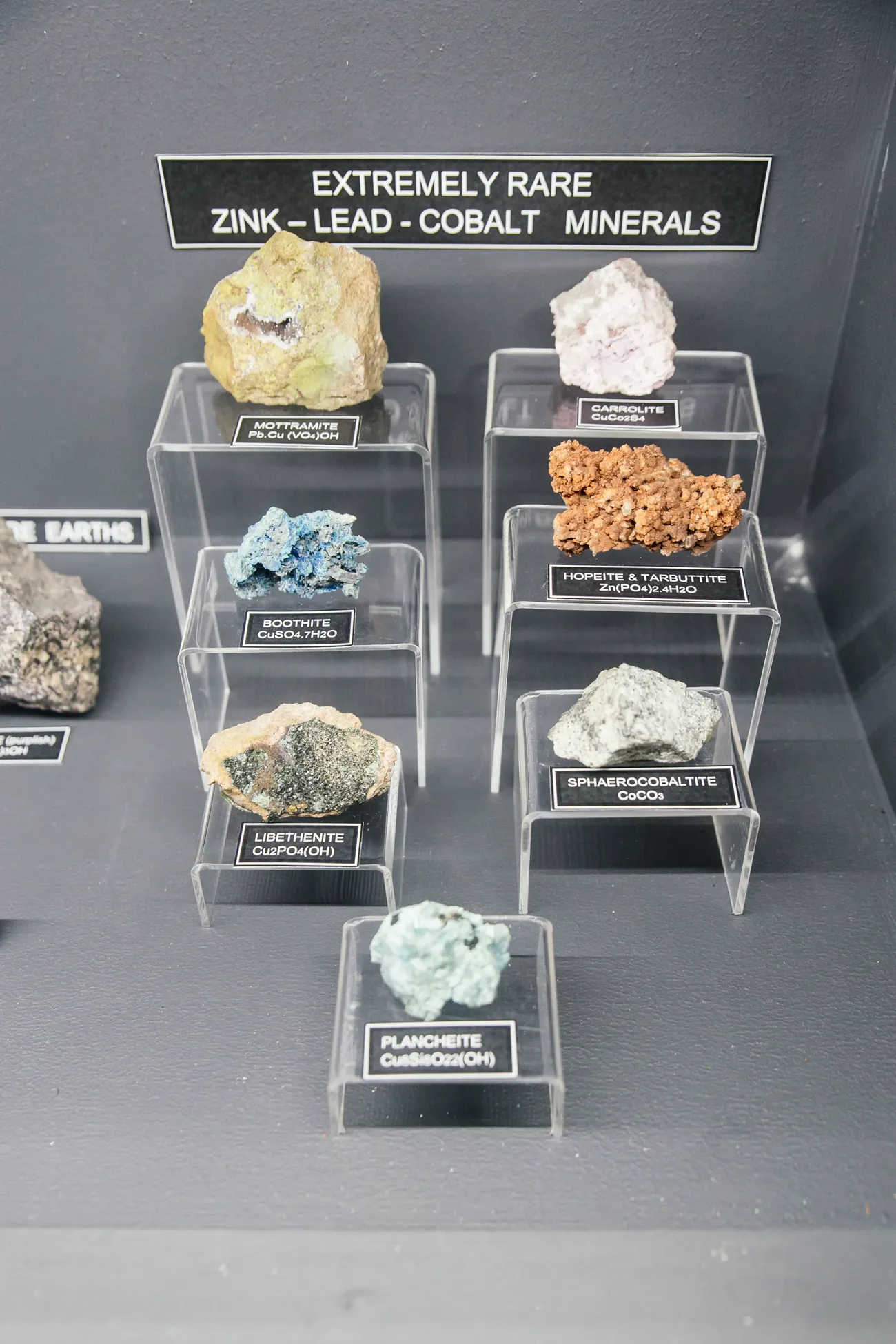 The rare zinc-lead-cobalt minerals cabinet in the museum: eight specimens (Mottramite, Carrolite, Boothite, Hopeite, Tarbuttite, Libethenite, Sphaerocobaltite and Plancheite) labelled with chemical formulae on acrylic plinths