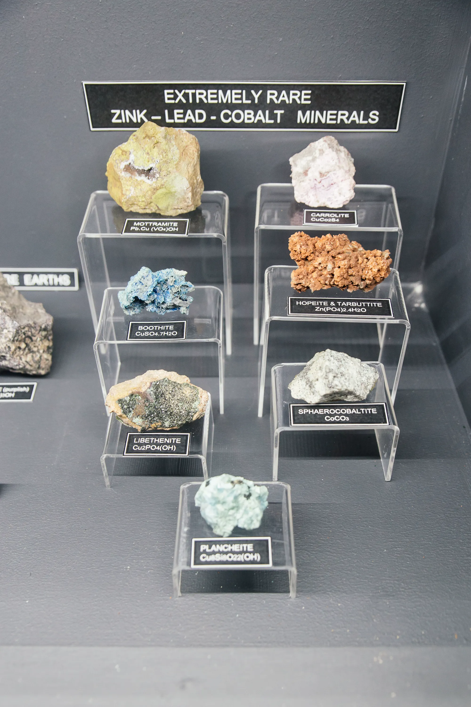 The rare zinc-lead-cobalt minerals cabinet in the museum: eight specimens (Mottramite, Carrolite, Boothite, Hopeite, Tarbuttite, Libethenite, Sphaerocobaltite and Plancheite) labelled with chemical formulae on acrylic plinths